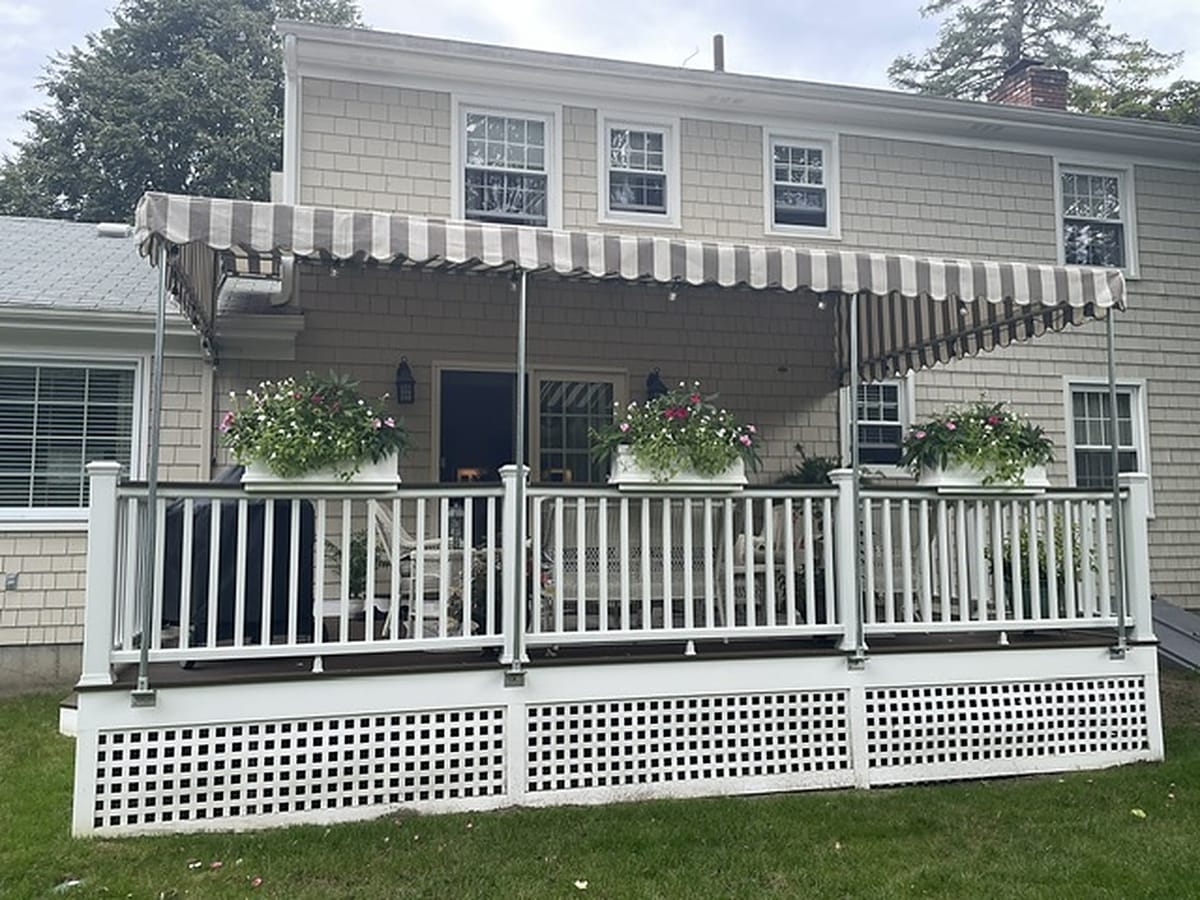 Tan and white striped stationary awning over a rear deck with white railings and flower boxes
